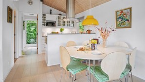 Une cuisine moderne avec des meubles blancs, un luminaire suspendu jaune et un coin repas comprenant une table ronde et des chaises.