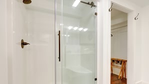 Une salle de bain moderne avec une douche à parois de verre, un lavabo blanc et un étendoir à linge en bois.