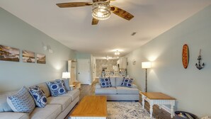 A spacious living room with a sofa, coffee table, and a ceiling fan. A kitchen is visible in the background. - 'better Lake Than Never' Huddleston Condo (Huddleston)