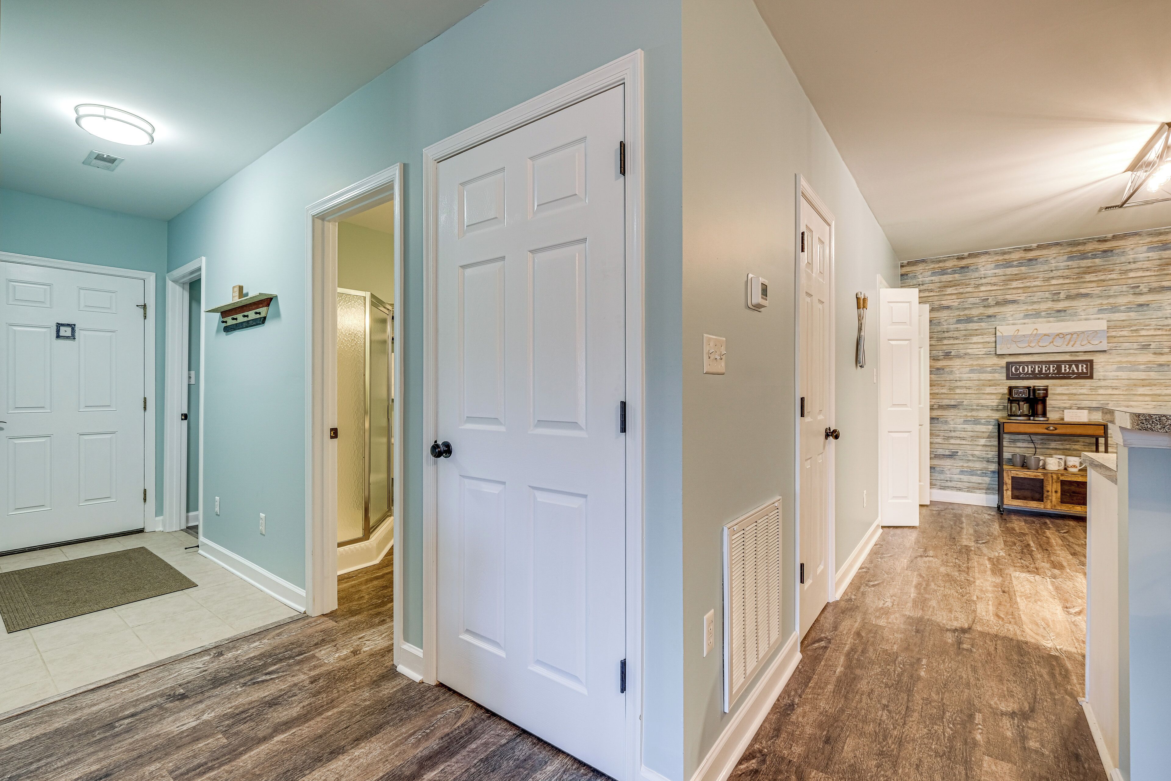 A hallway with white doors, a welcome sign, and a coffee bar area.