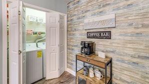 A laundry room with a washing machine and dryer, a coffee bar with a coffee maker and mugs, and a welcome sign on the wall. - 'better Lake Than Never' Huddleston Condo (Huddleston)