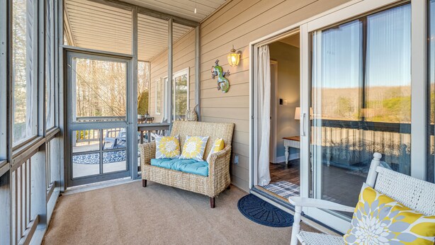 A covered porch with a wicker sofa, a white bench, and a glass door leading to a patio. - 'better Lake Than Never' Huddleston Condo (Huddleston)