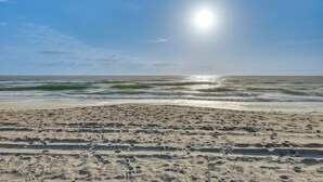 Ein Strand mit Fußspuren, die zum Wasser führen, Wellen und einem klaren Himmel.