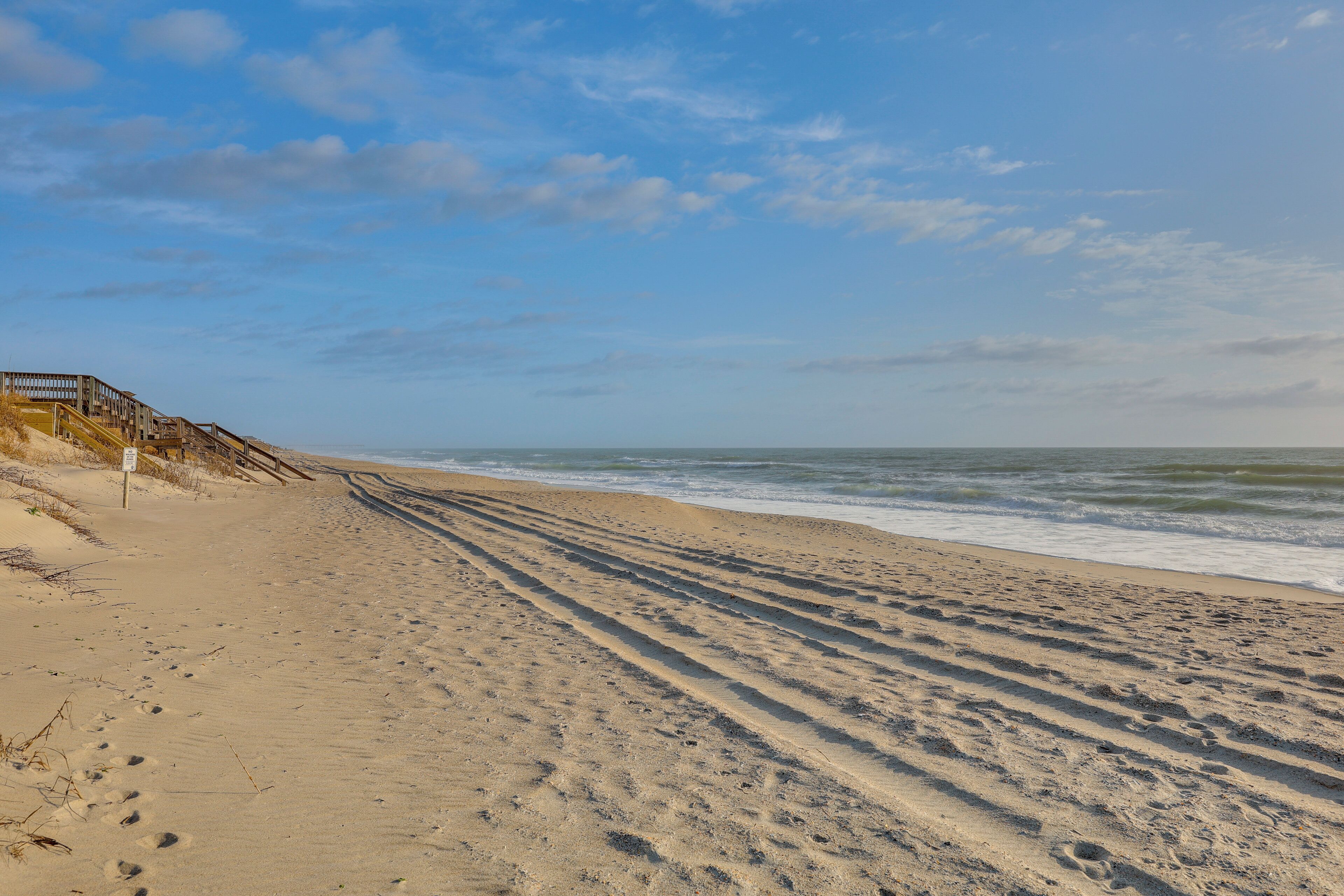 A sandy beach with footprints leading to a wooden staircase.