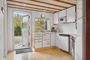 A modern kitchen with white cabinets, a clock, a window, and a door leading outside. - Lovely holiday home in Pøt Strandby (Juelsminde)