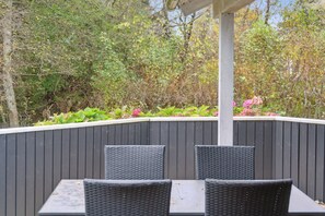Eine Terrasse im Freien mit Tisch und Stühlen, umgeben von einem Holzzaun und viel Grün.