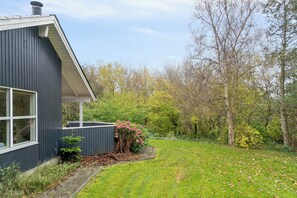 A modern house with a dark exterior, a visible window, and a garden with trees and shrubs. - Lovely holiday home in Pøt Strandby (Juelsminde)