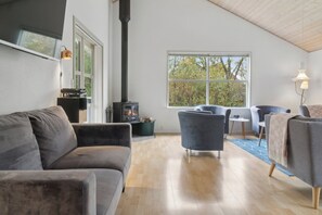 A modern living room with a sofa, armchairs, a fireplace, and a large window. - Lovely holiday home in Pøt Strandby (Juelsminde)
