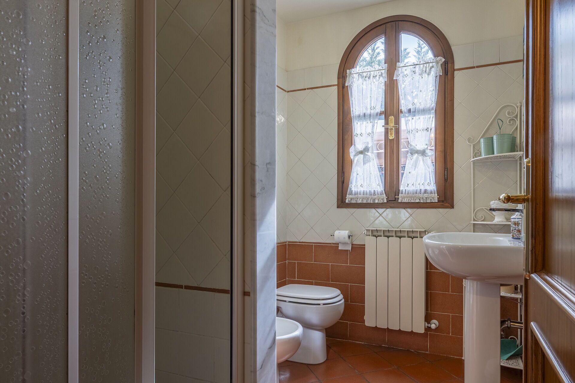 A bathroom with a toilet, sink, and a window with a curtain.