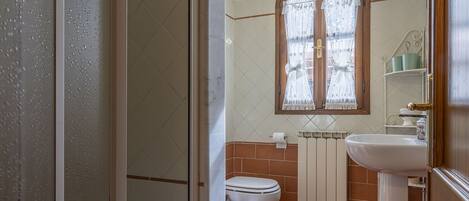A bathroom with a toilet, sink, and a window with a curtain.