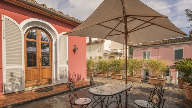 Un patio al aire libre con una mesa y sillas, rodeado de macetas con plantas y un paraguas grande.