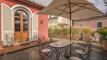 Une terrasse extérieure avec une table et des chaises, entourée de plantes en pot et d’un grand parasol.