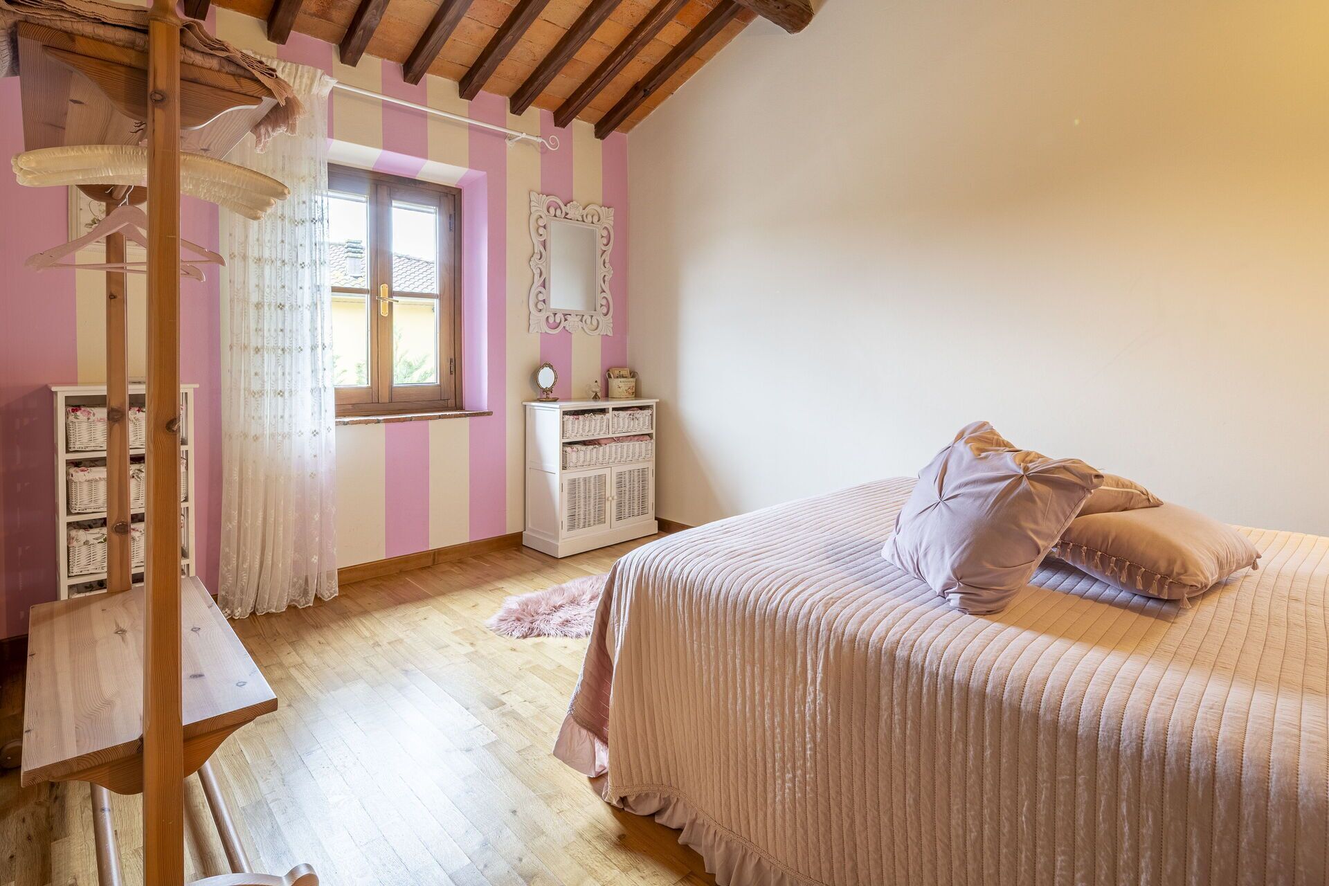 Une chambre à coucher comprenant un lit, une coiffeuse avec un miroir, une armoire et une fenêtre avec des rideaux.