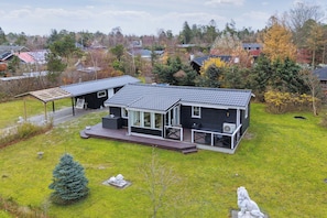 A modern house with a large deck, a covered patio, and a well-maintained lawn.