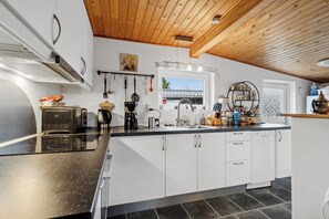 A modern kitchen with white cabinets, a black countertop, and a wooden ceiling. - Holiday idyll near beach and city life (Hals)