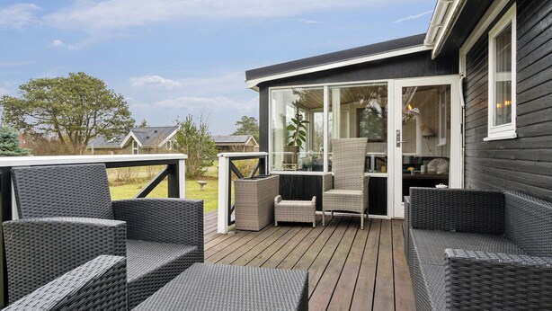 A deck with wicker furniture, a glass door leading to a room, and a view of the surrounding area. - Holiday idyll near beach and city life (Hals)