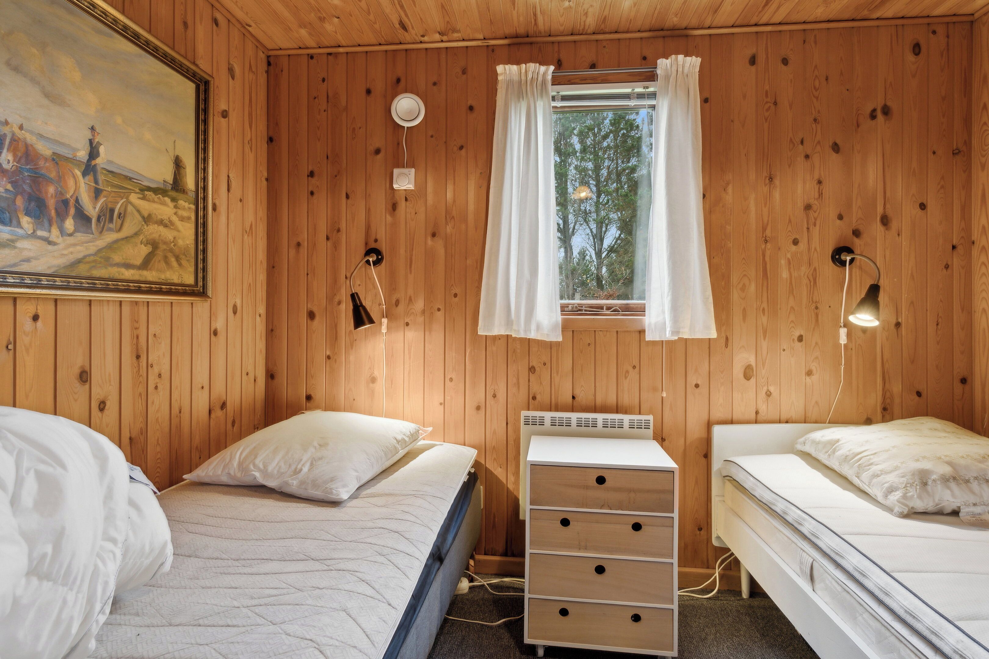 Een kamer met houten lambrisering, twee bedden, een dressoir, een schilderij, een raam met gordijnen en wandlampen.