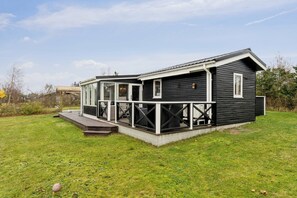 A black wooden cabin with a glass door entrance, a deck, and a small porch. - Holiday idyll near beach and city life (Hals)