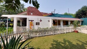 A house with a white picket fence, a red roof, and a green tarp covering part of the structure. - Koko's Farm (Mohanlalganj)