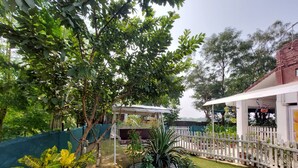 A garden with a swing, a white fence, and a building with a red roof. - Koko's Farm (Mohanlalganj)