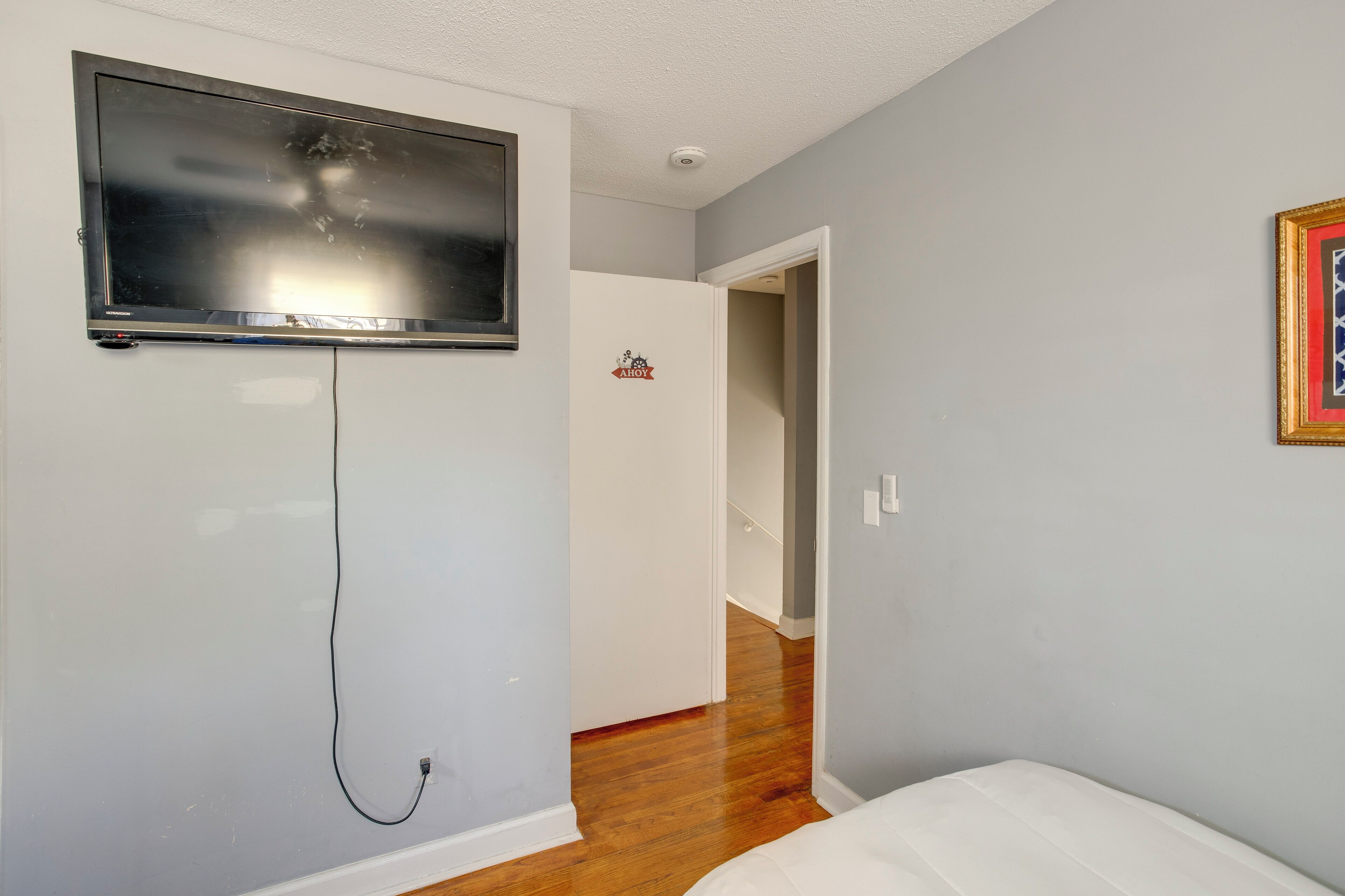 A room with a mounted TV, a door with a 'HOY' sign, and a framed picture on the wall.