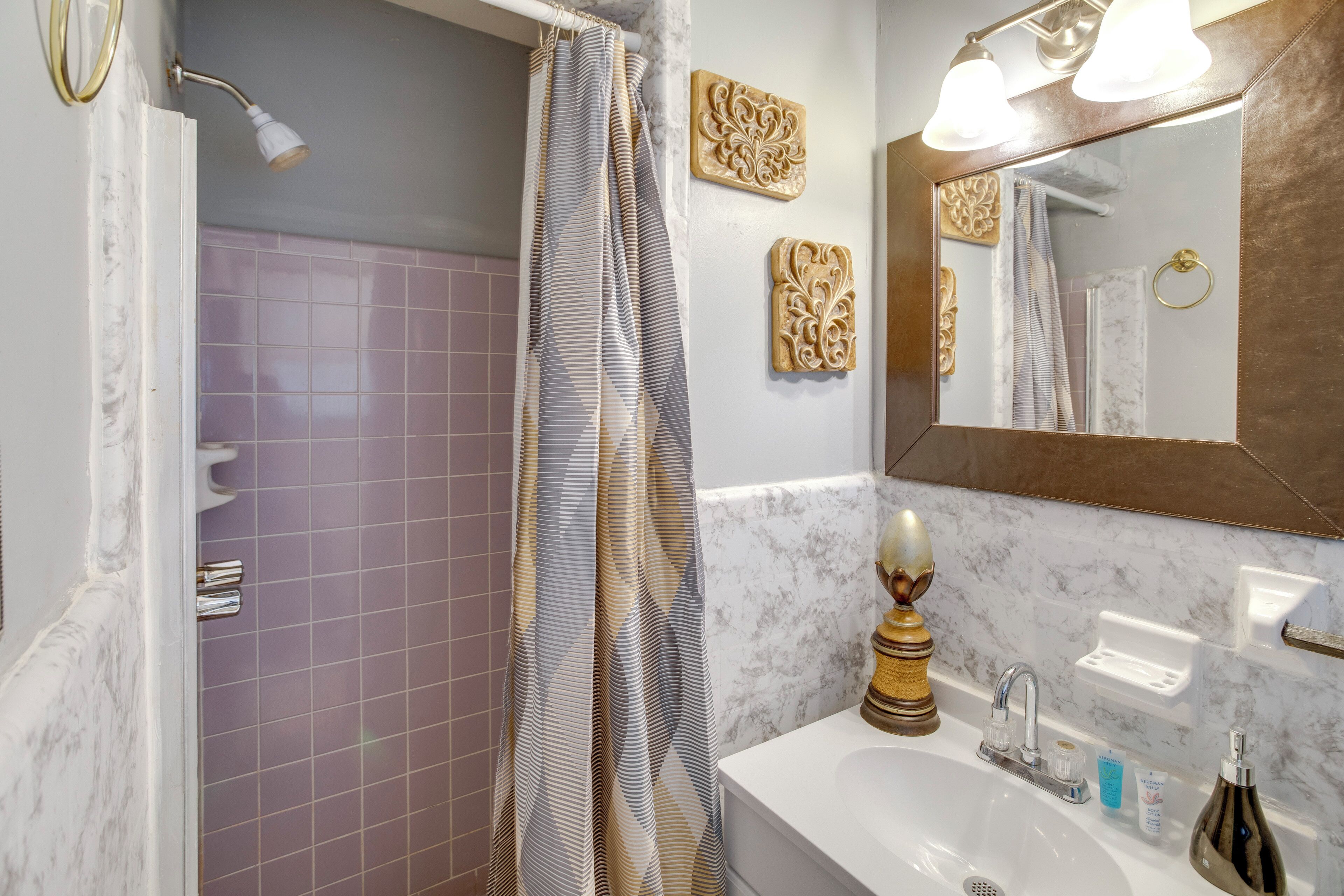 Een badkamer met een douche, wastafel, spiegel en decoratieve wanddecoraties.