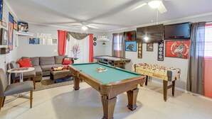 Una sala de estar con mesa de billar, mesa de futbolín, sofá y televisor.