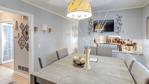 Un comedor con una mesa de madera, sillas tapizadas en gris, un florero con adornos y una lámpara de techo moderna.