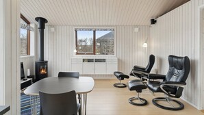 Ein modernes Interieur mit einem runden Tisch, schwarzen Ledersesseln, einem eingebauten Kamin und einem Fenster mit Blick auf Bäume.