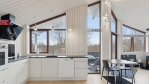 Eine moderne Küche mit einer großen Kochinsel, eingebauten Geräten und großen Fenstern mit Blick ins Freie.