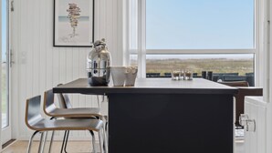 A modern kitchen with a central island, white walls, and a large window offering a view. - Cozy holiday home on Orø (Orø)