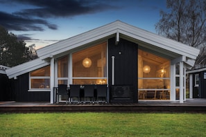 Et moderne hus med store vinduer, en terrasse og et spiseområde.