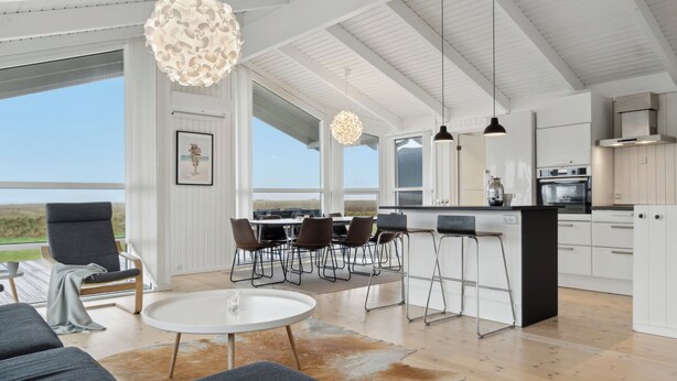 A modern kitchen with white cabinetry, a central island, and a dining area with chairs and a table. - Cozy holiday home on Orø (Orø)