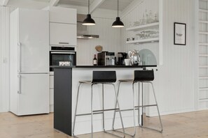 Une cuisine moderne avec des meubles blancs, un plan de travail noir et trois tabourets de bar.