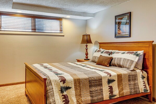 A bedroom with a wooden bed, a nightstand with a lamp, a window with blinds, and a framed picture on the wall. - 180° Mtn Views, Hot Tub, Game Room: Cobbly Nob Gem (Gatlinburg)