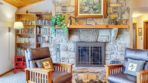 Ein gemütliches Wohnzimmer mit Kamin aus Stein, Ledersesseln und einer Bücherwand voller Bücher.