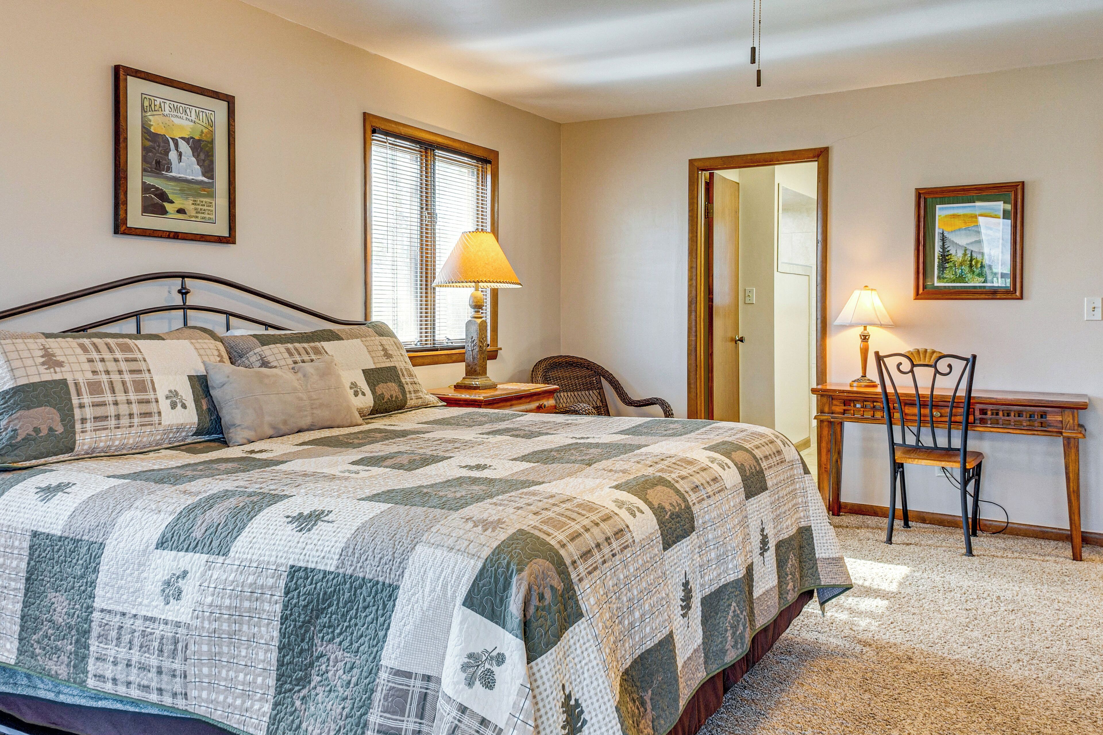 A bedroom with a large bed, two bedside lamps, a chair, and a desk.