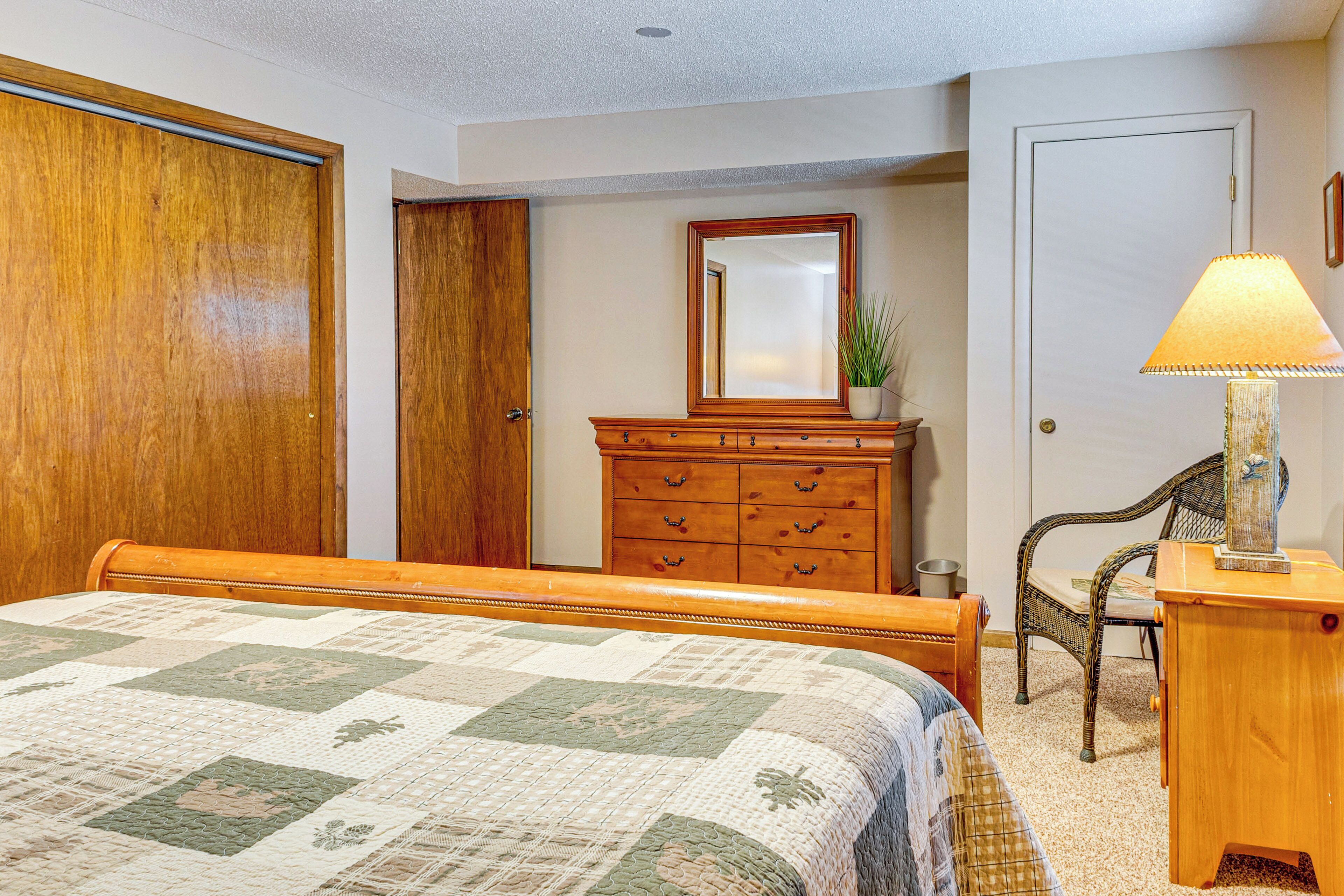 A bedroom with a wooden bed, a dresser, a chair, and a lamp.