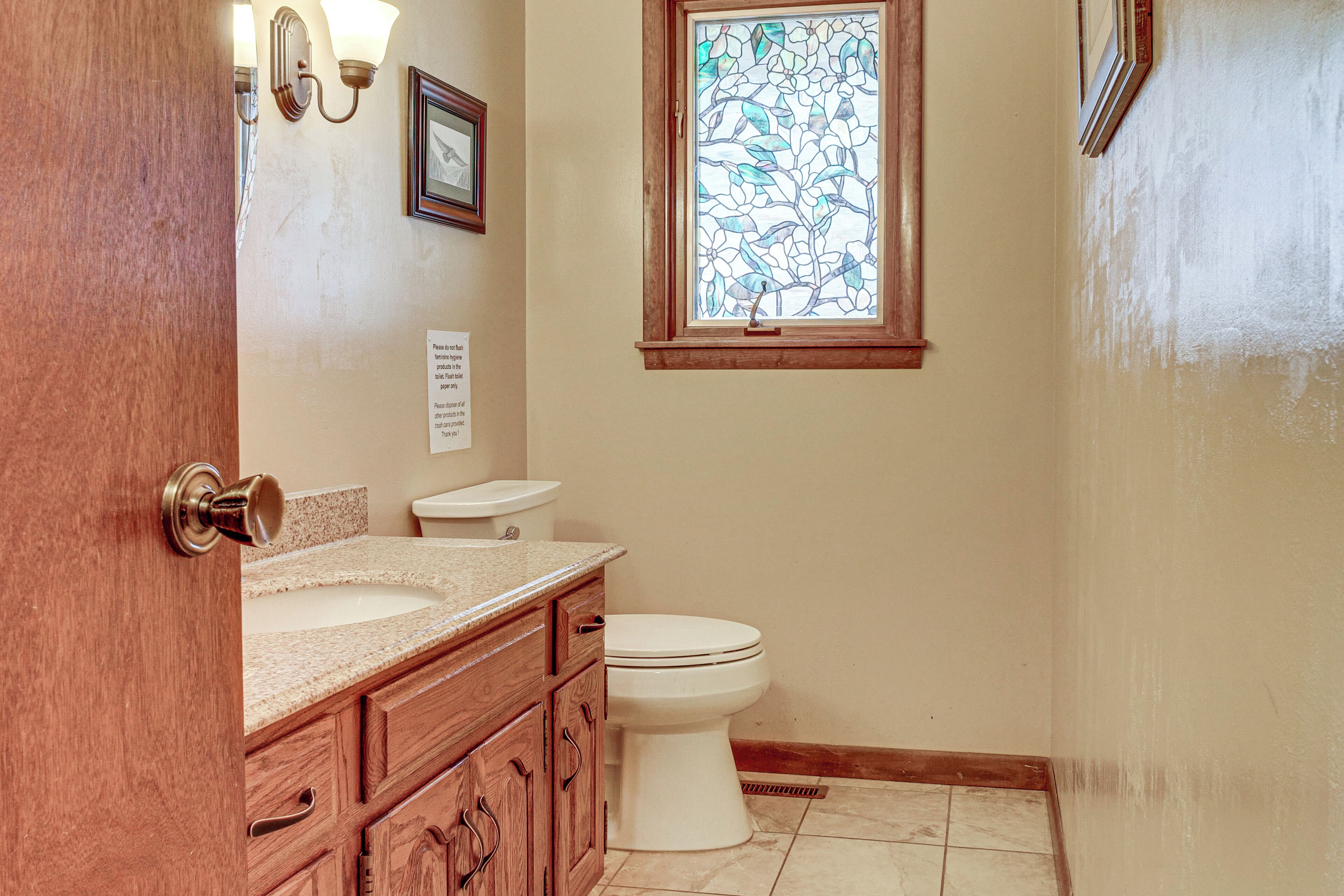 A bathroom with a wooden vanity, a white toilet, a stained glass window, and a wall-mounted light fixture.