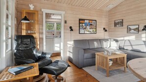 A cozy cabin interior with a leather chair, grey sofa, wooden coffee table, and a bookshelf.