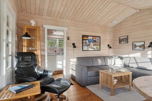 L’intérieur d’un chalet chaleureux, avec un fauteuil en cuir, un canapé gris, une table basse en bois et une bibliothèque.