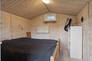 Ein Zimmer mit Holzwänden, einem Bett, einem kleinen Fenster, einer Gitarre und einem weißen Schrank.