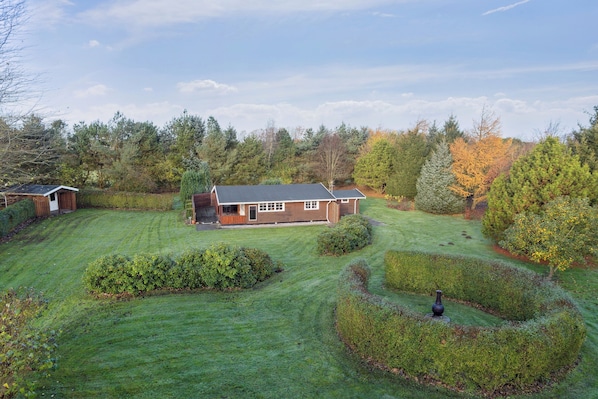 Ein Haus mit gepflegtem Rasen, einer kleinen Gartenhütte und einem Garten mit ordentlich geschnittenen Sträuchern.