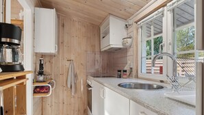A compact kitchen with wooden walls, a countertop, a sink, and a window.