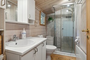 Une salle de bain avec un lavabo blanc, des toilettes et une douche fermée par des parois en verre.