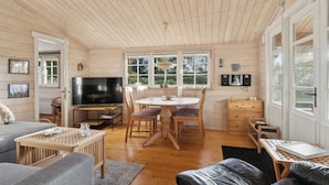 A cozy cabin interior with a wooden ceiling, a dining area with a table and chairs, a sofa, a TV, and a fireplace.