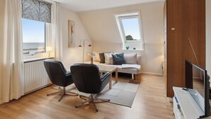 Une chambre moderne avec vue sur la mer, comprenant un canapé, deux fauteuils, un téléviseur et un plancher en bois.