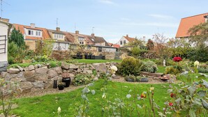 Un jardin résidentiel avec des murs en pierre, une grande variété de plantes et un ciel dégagé.