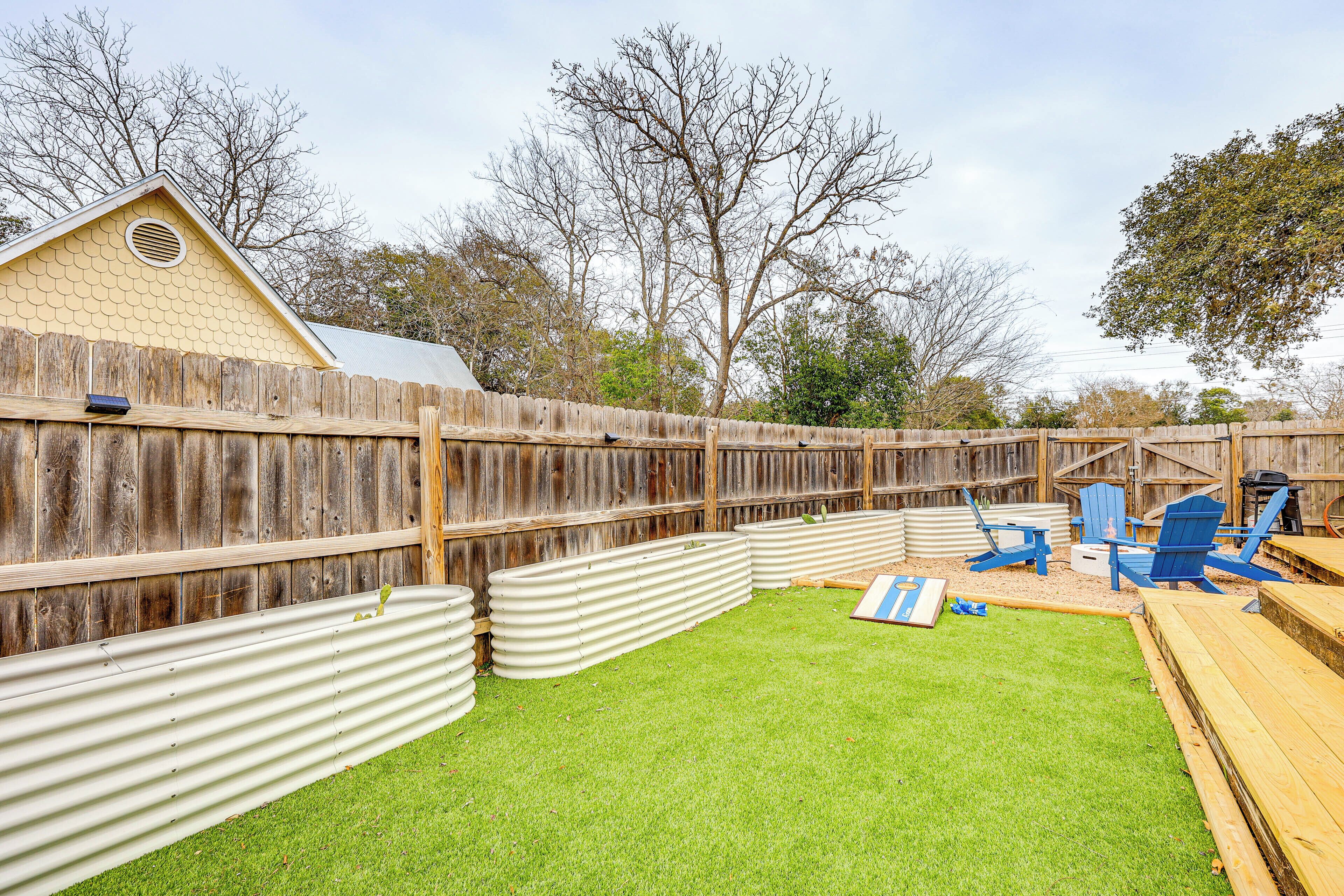 A backyard with a wooden fence, a small shed, and blue Adirondack chairs.