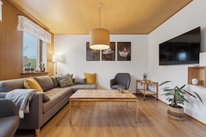 A modern living room with a sofa, coffee table, and a television mounted on the wall. - Spacious holiday home near the beach (Bagenkop)